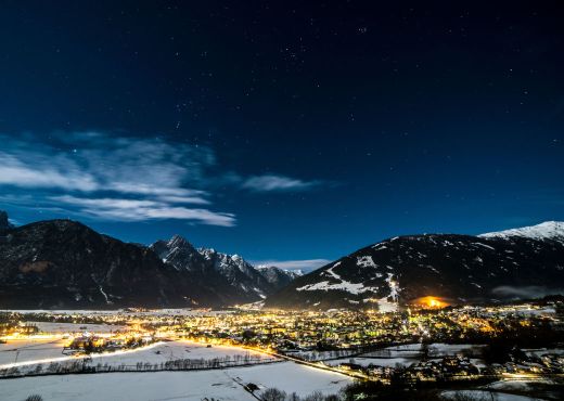 Winternacht in Lienz. Dunkelblauer Himmel, es liegt Schnee im Tal und Häuser sind beläuchtet.