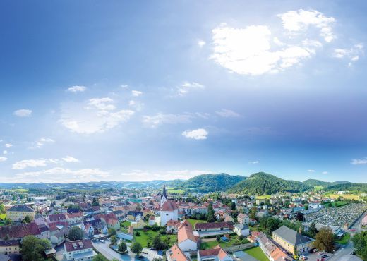 Blick auf die Stadt von oben mit grün bewaldeten Hügeln und strahlend blauem Himmel im Hintergrund