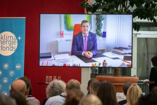 Videobotschaft des Ministers auf der Leidwand vor Publikum