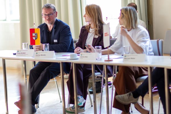 Personen sitzen um einen Tisch und sprechen miteinander