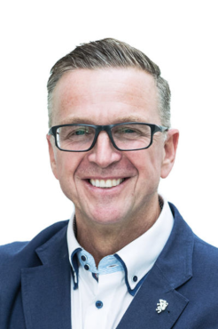 Porträt eines lächelnden Mannes mit Brille, der ein weißes Hemd und eine blaues Jacket trägt