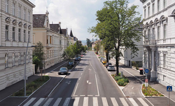 Dreispurige Straße in der Stadt Krems, daneben Parkplätze, Bäume und Wohnhäuser