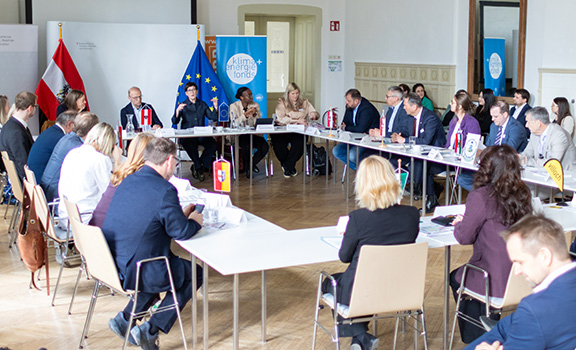 Ca. 30 Personen sitzen rund um einen Tisch und sprechen miteinander