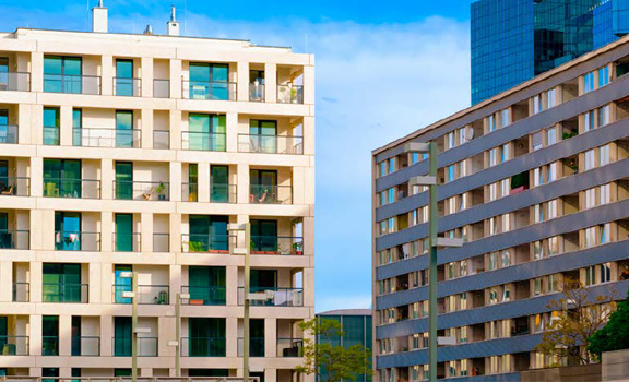 Mehrstöckige Wohngebäude mit vielen Fenstern und Balkonen vor blauem, leicht bewölktem Himmel